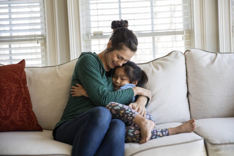 Mother and daughter snuggling on sofa