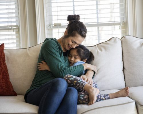 Mother and daughter snuggling on sofa