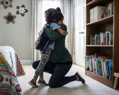 Mother embracing young daughter before school